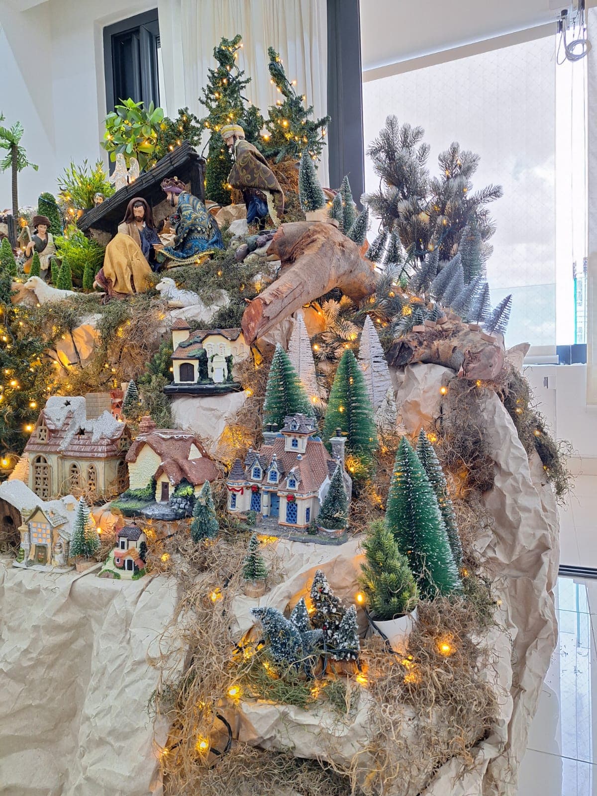 Villa en miniatura sobre una montaña de musgo y driftwood, con casas iluminadas.