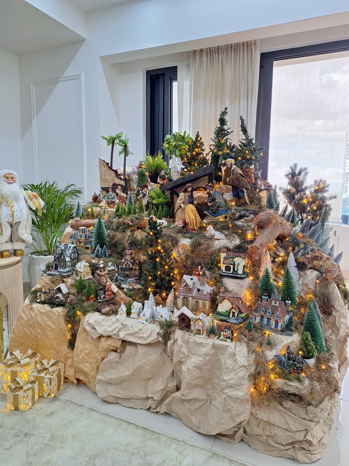 Vista amplia de un belén con palmeras, regalos y una villa navideña completa.